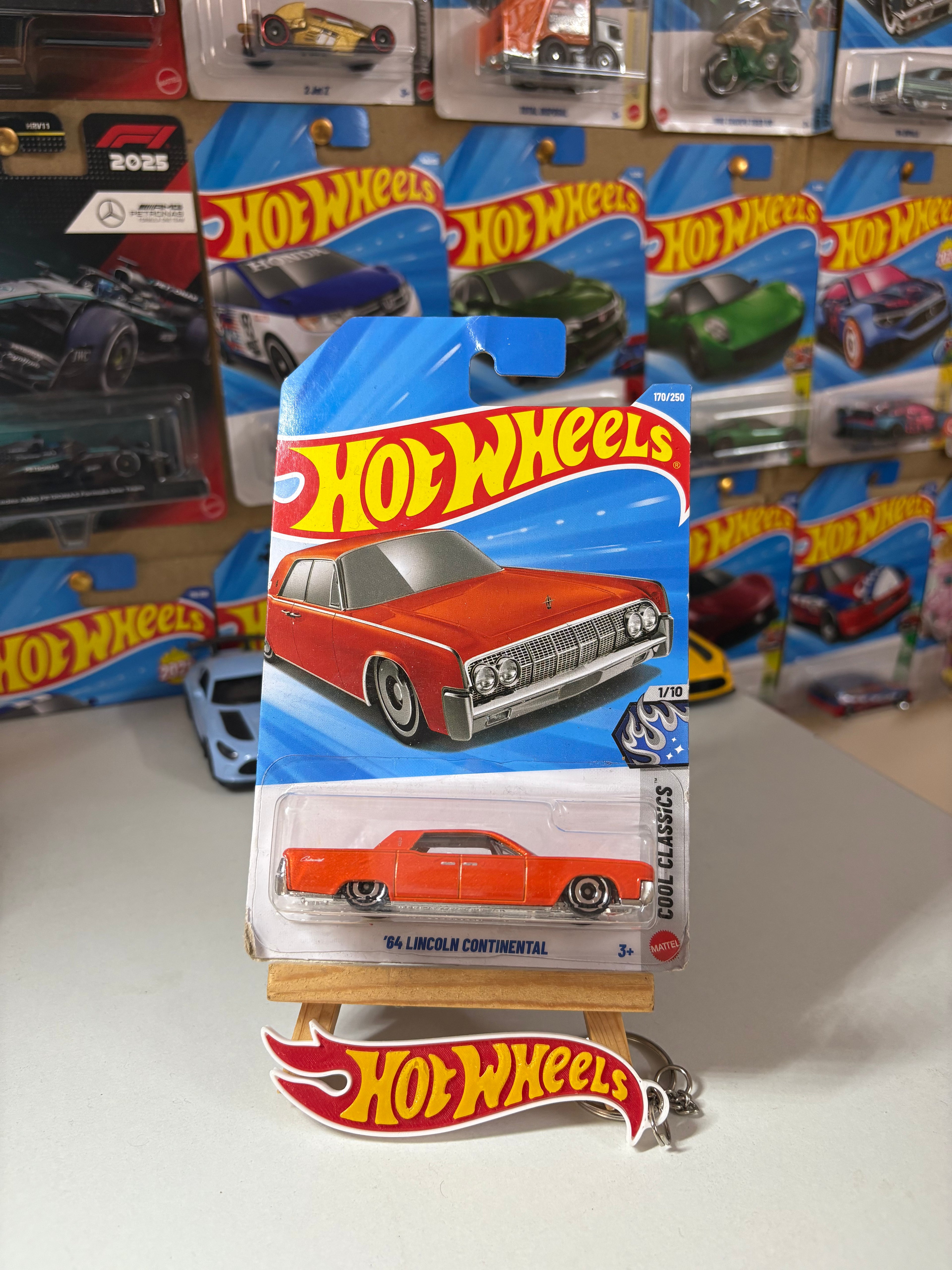 A Hot Wheels die-cast toy car in its original blister packaging, displayed on a small wooden stand with a Hot Wheels logo plaque. The carded packaging features a blue and red design with an illustration of the red 1969 Lincoln Continental.